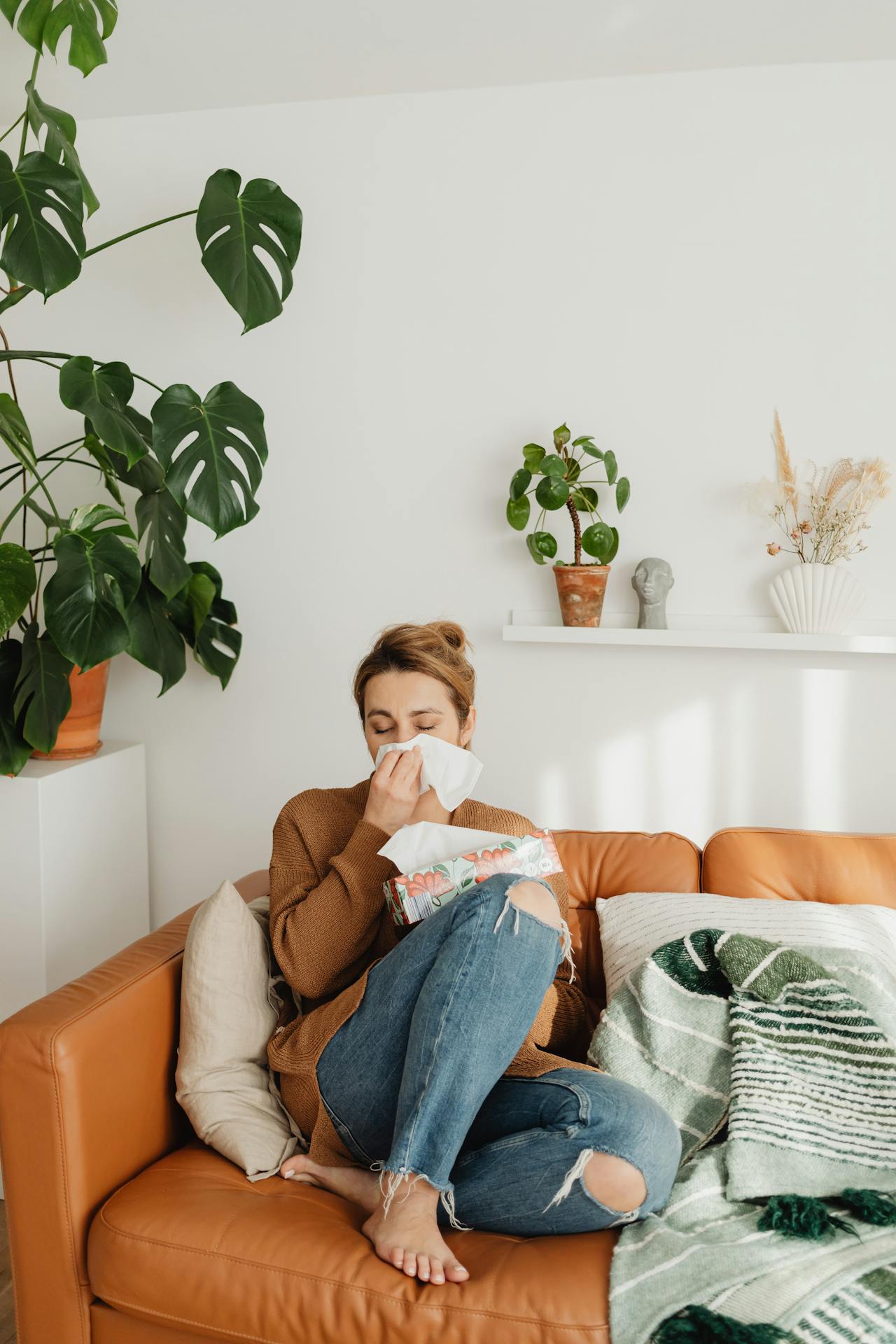 Woman sitting on couch with tissues, sneezing from allergies at home highlighting the need for clean, allergen-free spaces.